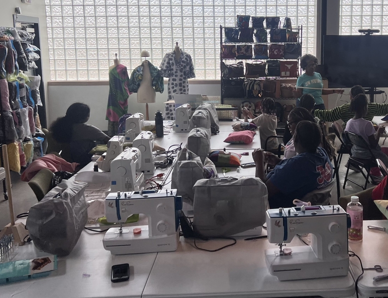 A group of students seated at sewing machines give attention to the instructor.